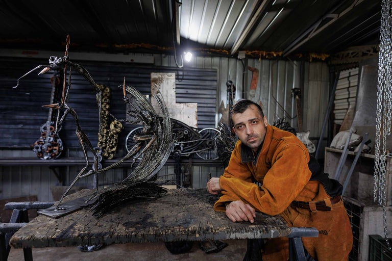 Bărbat în haine de lucru lângă o sculptură metalică într-un atelier