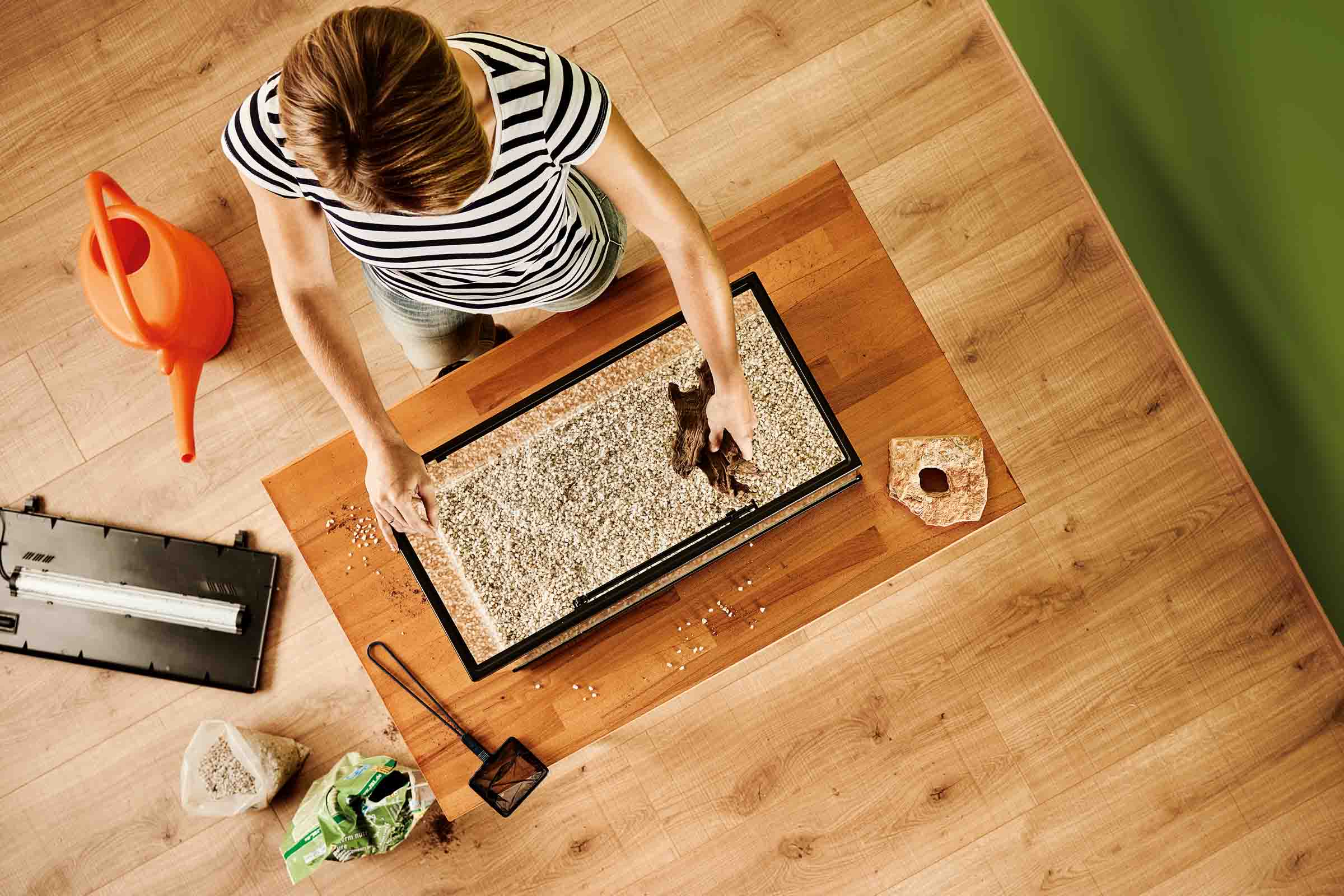 Amenajare acvariu cu elemente decorative, substrat și femeie la lucru