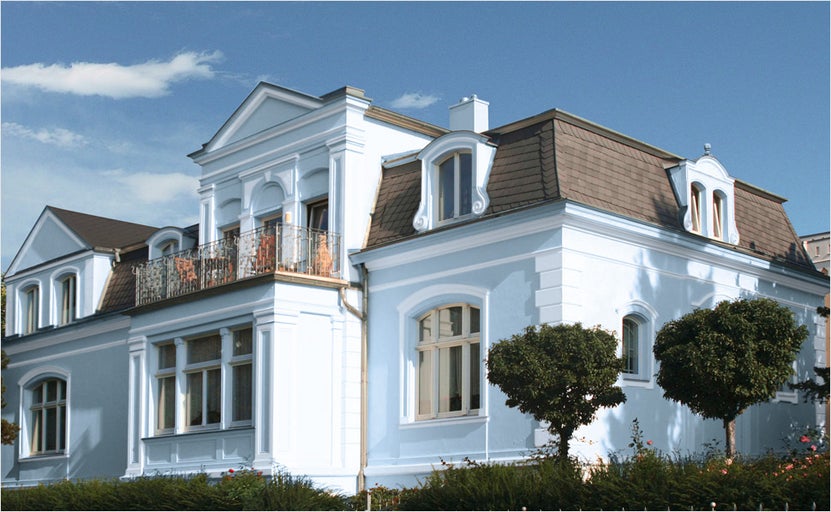 Vedere a unei case cu mai multe etaje, cu acoperiș tip mansardă, balcon și amenajare peisagistică a grădinii