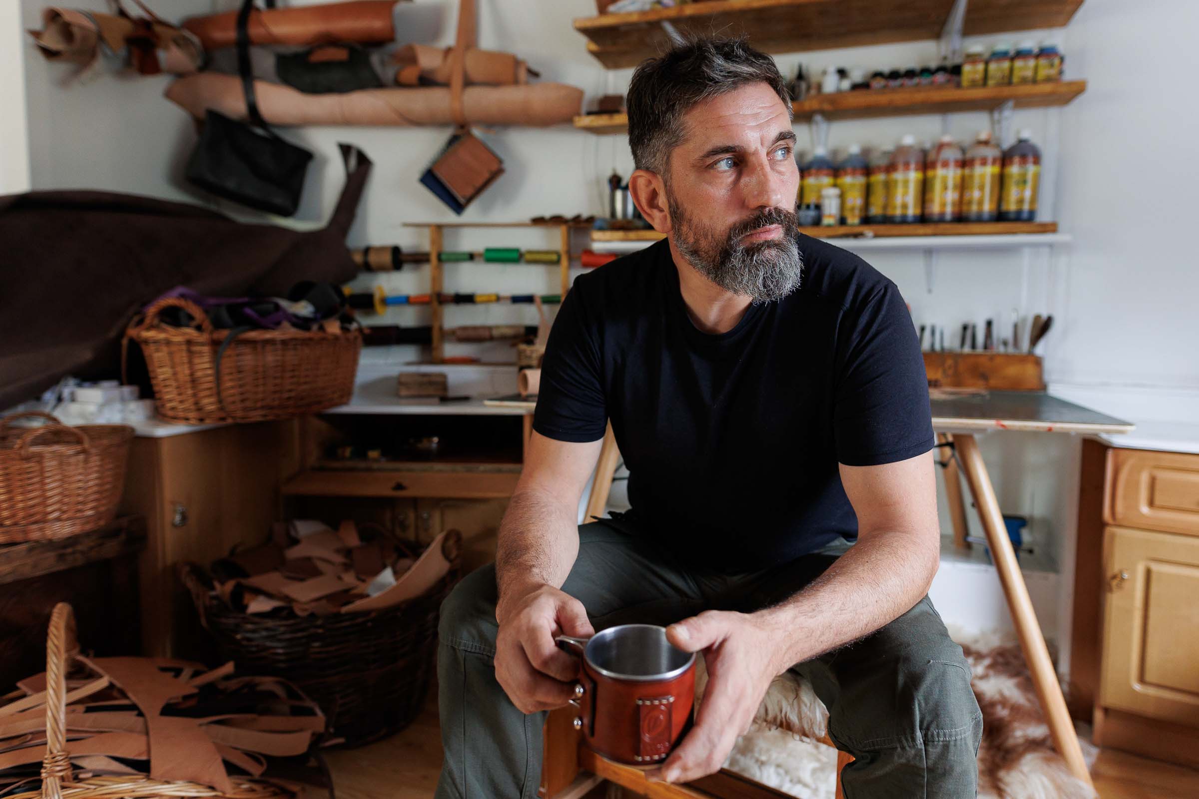 Bărbat stând cu o cană într-un atelier cu articole de artizanat din piele
