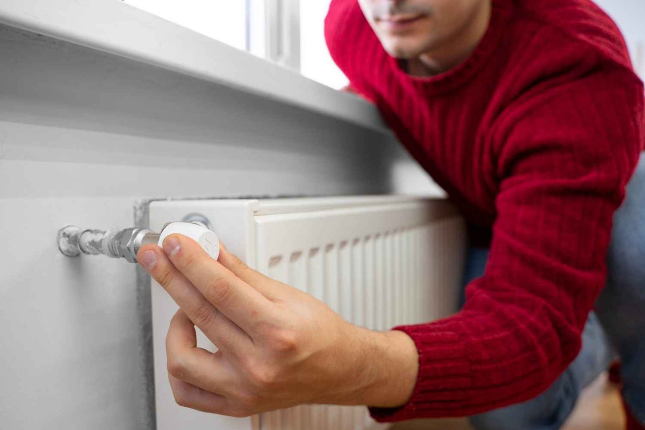 Bărbat reglează termostatul caloriferului