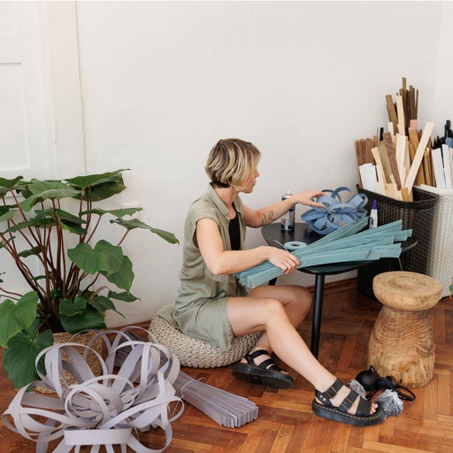 Femeie creează obiecte decorative cu fâșii de lemn pe podea.