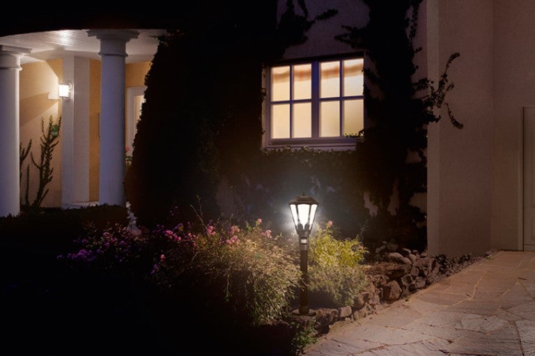 Grădină iluminată cu o lampă de grădină și o casă rezidențială în fundal
