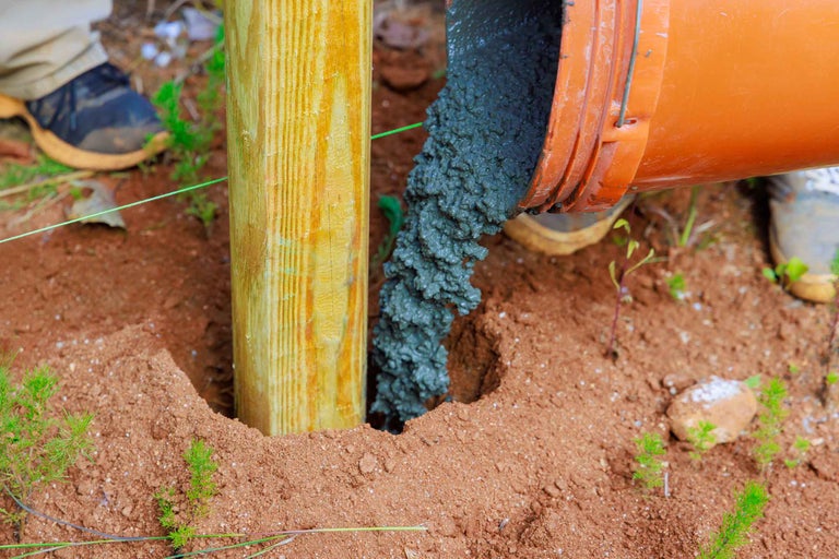 Betonul este turnat dintr-o găleată în jurul unui stâlp de lemn.