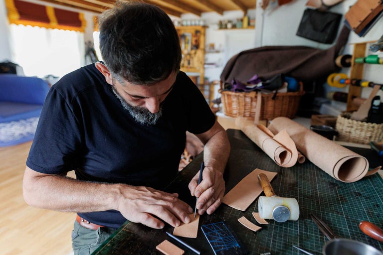 Un bărbat lucrează la o masă cu piele, unelte și un ciocan.