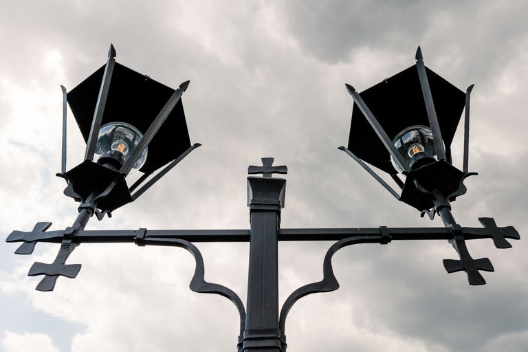 Un stâlp de iluminat stradal dublu cu becuri și o cruce Lorena pe un cer înnorat