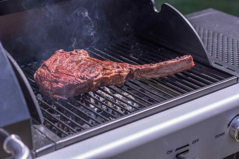 O friptură Tomahawk pe un grătar cu fum.