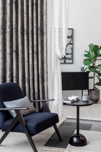 Cameră de zi cu scaun, măsuță laterală, comodă, plantă de interior, covor și perdele