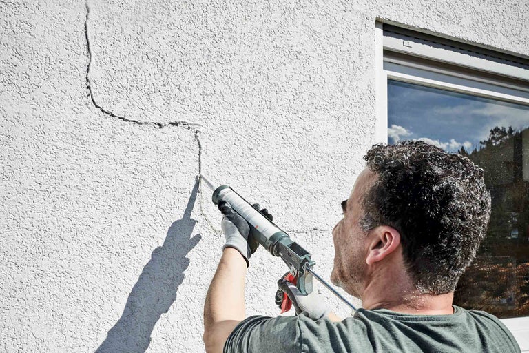 Un bărbat repară o fațadă cu un aplicator de etanșant.