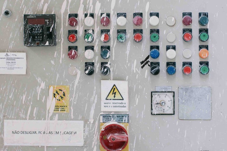 Panou de control industrial cu butoane colorate, întrerupătoare, afișaje digitale și simboluri de avertizare pentru tensiune electrică și întreținere.