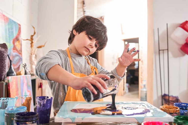 Copil turnând vopsea pe o pânză pentru un proiect de artă