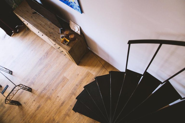 Zonă de zi modernă văzută de sus, cu o scară în spirală neagră, parchet laminat cu aspect de lemn și o comodă din lemn.