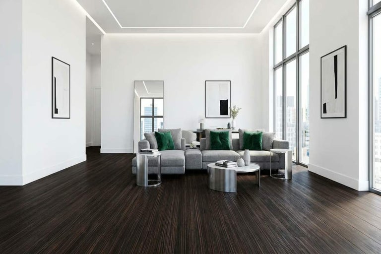 Cameră de zi luminoasă cu canapea gri, perne verzi și podea din lemn închis la culoare