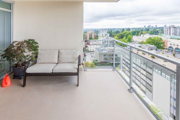 Balcon cu zonă de relaxare, plantă și balustradă de sticlă cu vedere spre oraș