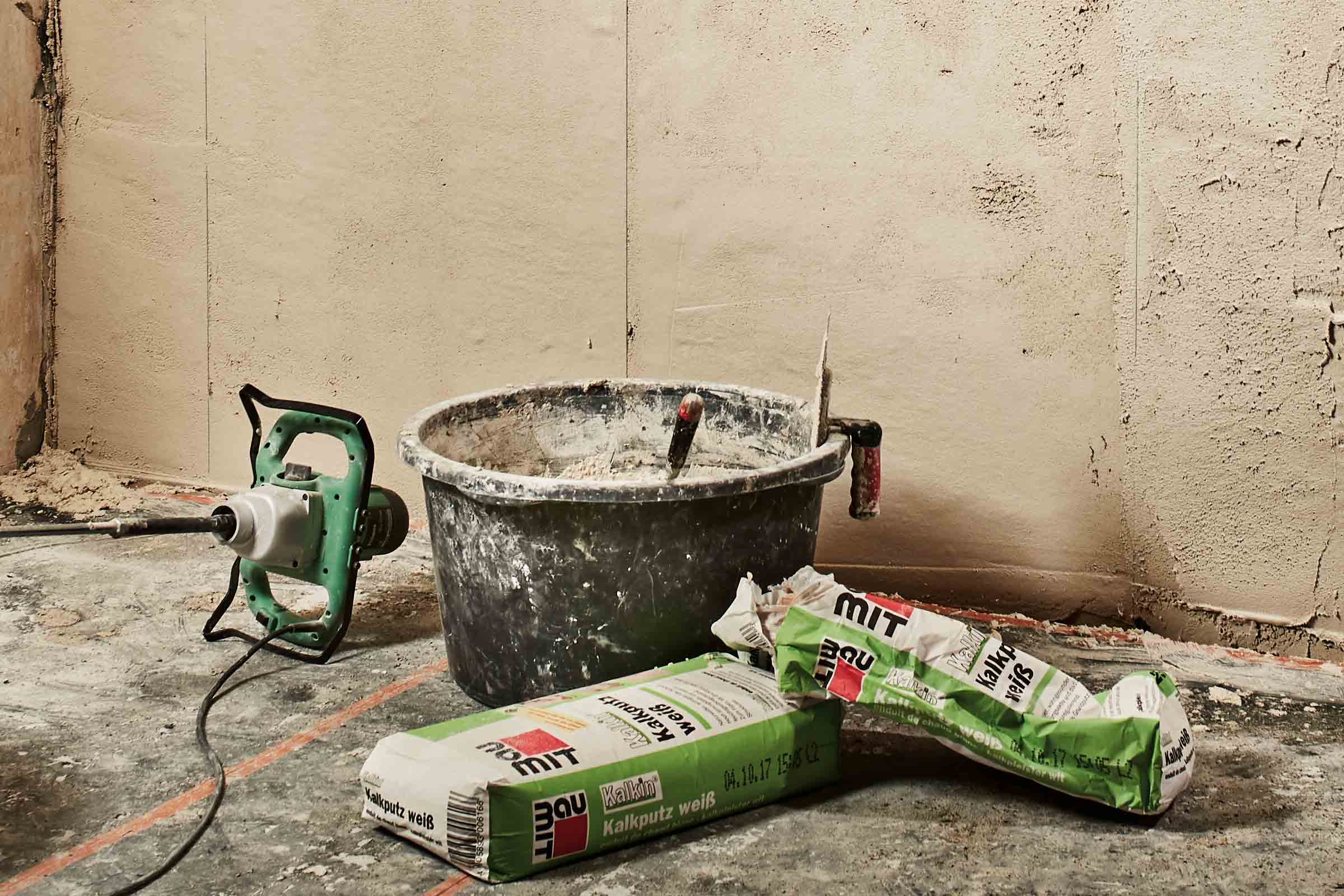 Scenă cu un mixer de mortar, o găleată, o mistrie și saci cu tencuială de var