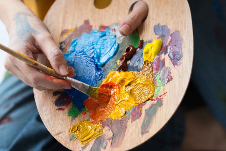 Paletă din lemn cu pete de culoare și pensulă în mână