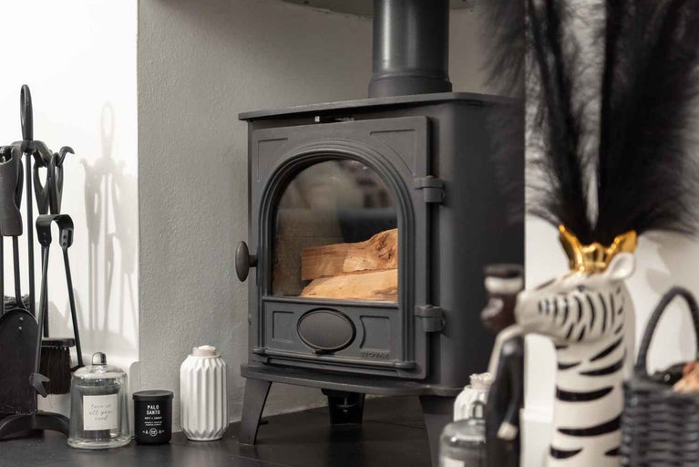 Șemineu cu lemne în camera de ardere, așezat pe o suprafață întunecată cu obiecte decorative