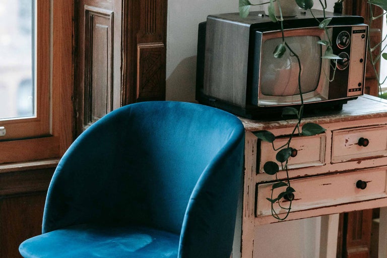 Scenă cu scaun de catifea albastră, televizor vintage și comodă în cameră.