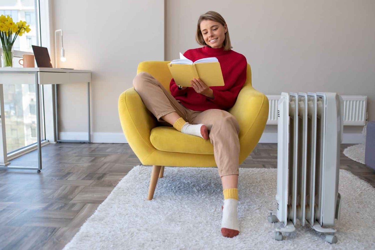 O femeie citește o carte într-un fotoliu galben lângă un radiator într-un living luminos și confortabil.