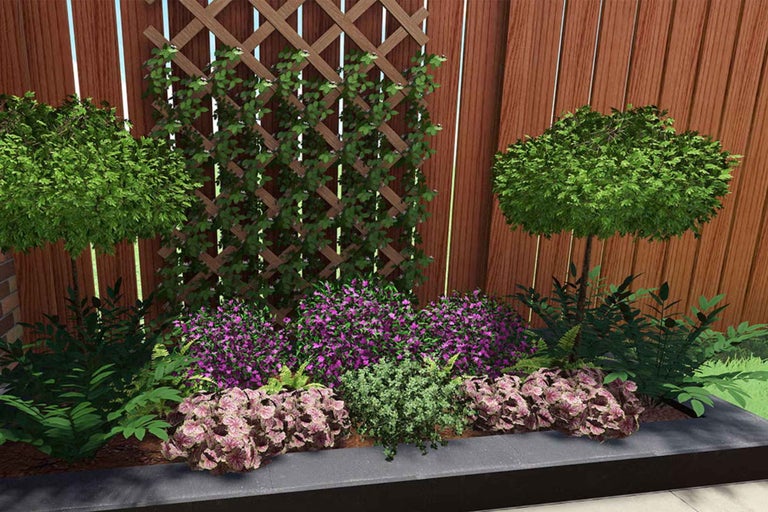 Strat înălțat plantat cu flori mov, plante cu frunze decorative și arbuști pe tulpină în fața unui gard de lemn cu spalier.