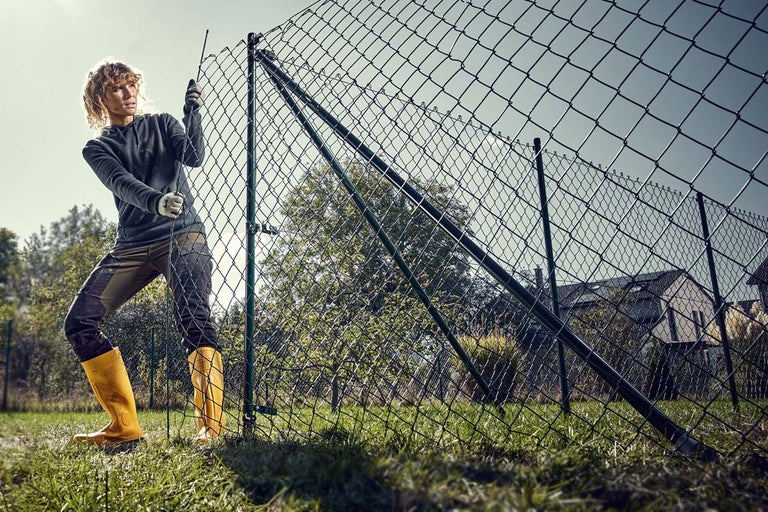 Femeie instalează un gard din plasă de sârmă în grădină.