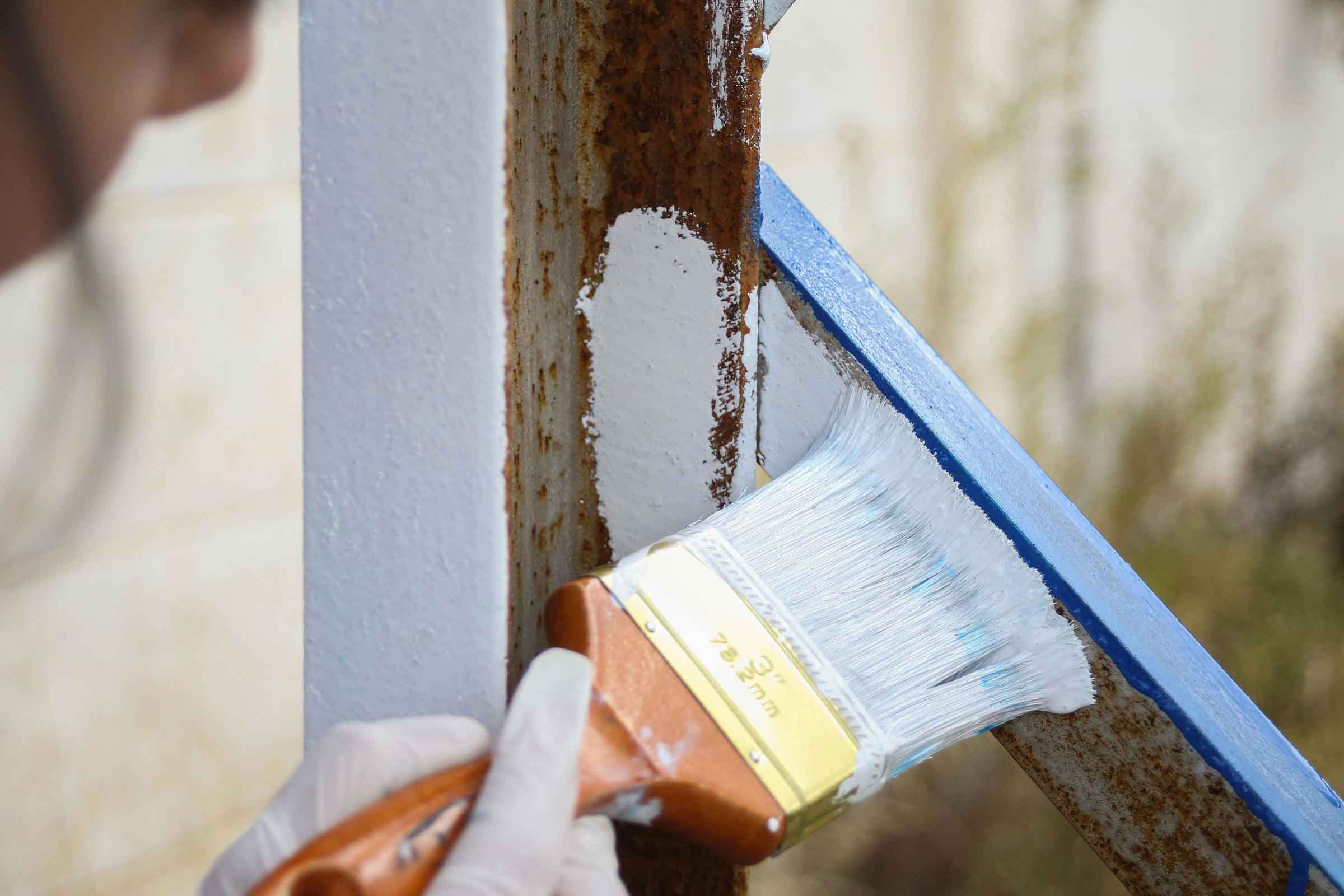O persoană poartă mănuși și vopsește o balustradă metalică cu o pensulă.