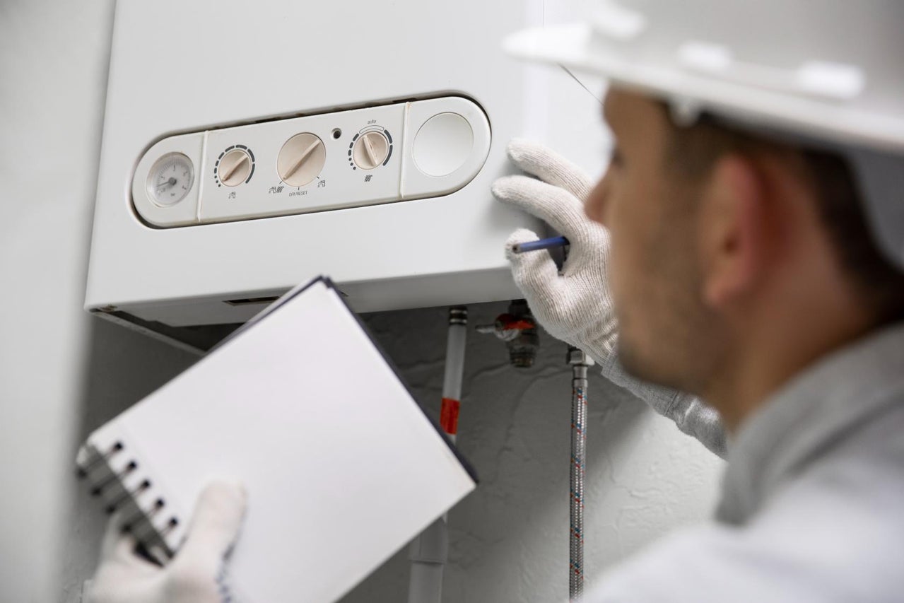Un instalator inspectează un sistem de încălzire cu un blocnotes.