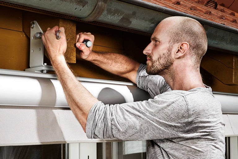 Un bărbat montează o rolă cu unelte pe o fereastră.