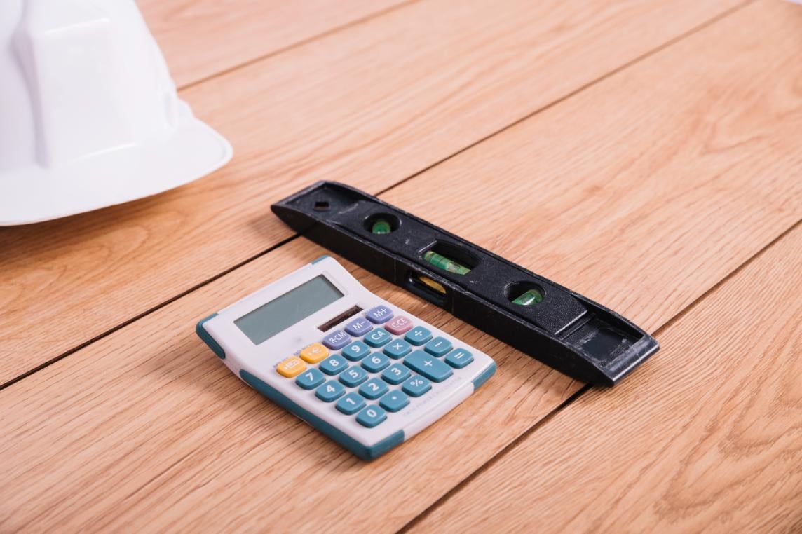 Calculator, nivelă și cască de protecție pe o pardoseală din lemn.