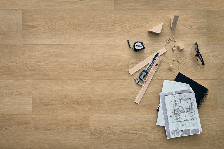Pardoseală din vinil cu aspect de stejar montată, cu plan de construcție, șubler, ruletă și mostre de lemn.