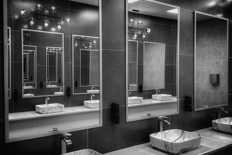 Design modern de baie cu lavoare pe blat din marmura, oglinzi patrate, baterii si lampi suspendate pe un perete placat cu gresie.