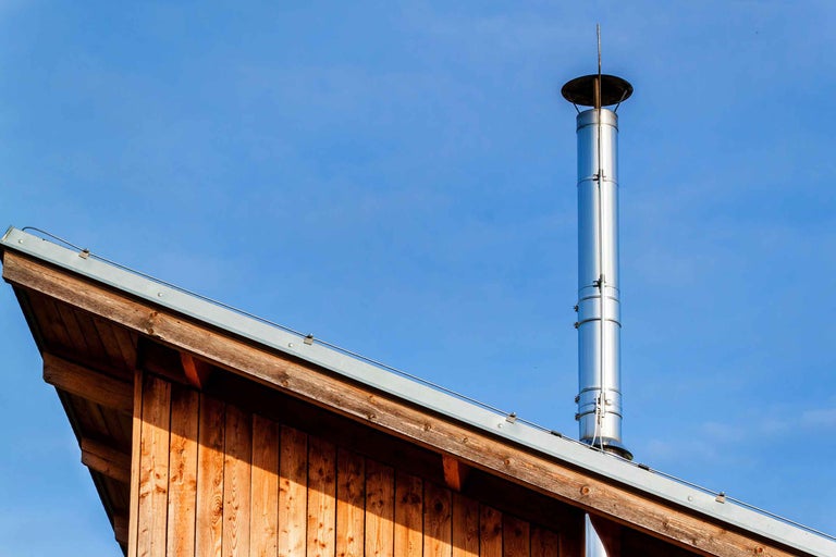 Coș de fum din oțel inoxidabil pe un acoperiș de lemn, pe fundalul unui cer albastru