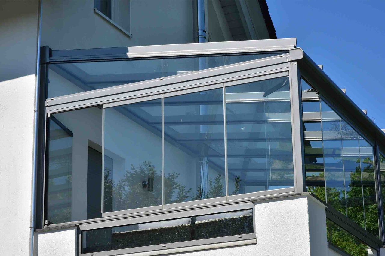Închidere modernă pentru balcon cu pereți glisanți din sticlă transparentă și profiluri robuste din aluminiu la o casă.
