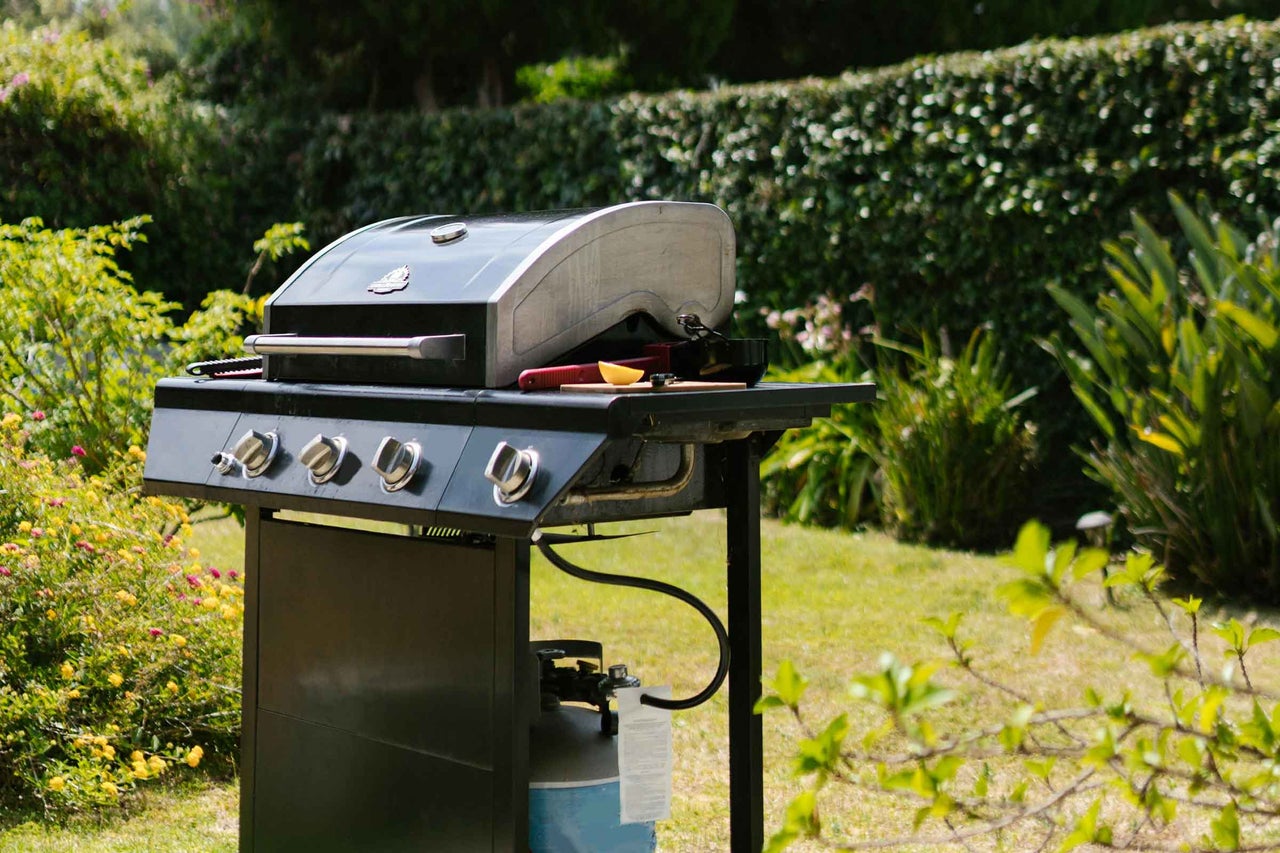 Grătar pe gaz cu patru arzătoare pe un gazon verde.