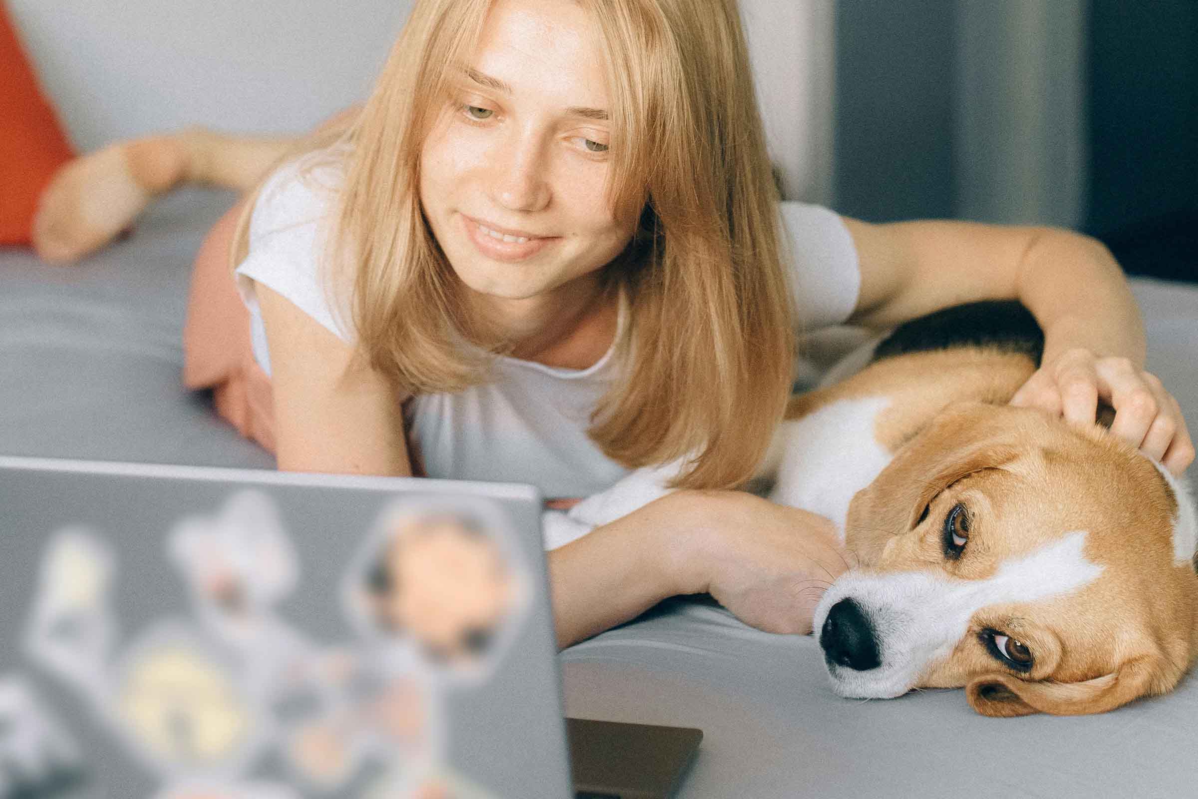 Femeie întinsă pe pat cu un câine și un laptop.