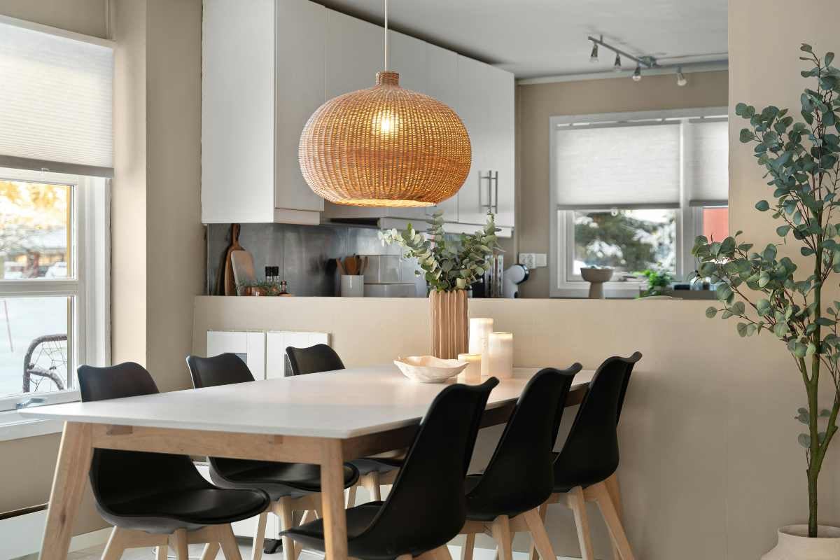 Lustră din ratan deasupra unei mese cu scaune negre într-o bucătărie luminoasă și modernă.