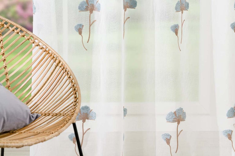 Șaluri decorative cu model floral lângă un scaun de ratan