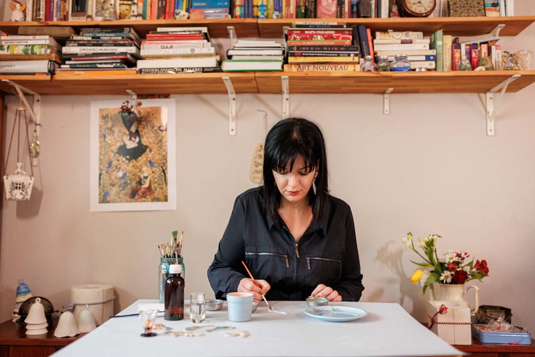 Femeie pictând ceramică într-un spațiu de lucru luminos, organizat, cu bibliotecă