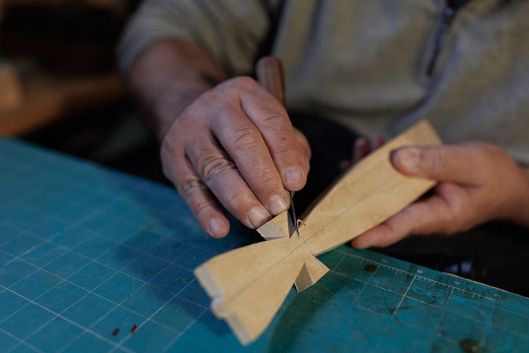 Un bărbat sculptează o bucată de lemn cu un cuțit pe o placă de tăiat