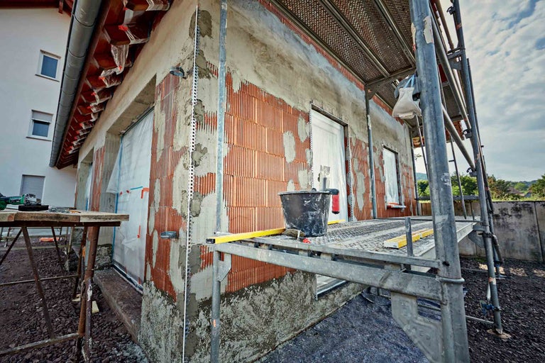 Exteriorul unei case în construcție cu schele, zidărie de cărămidă și lucrări de tencuială