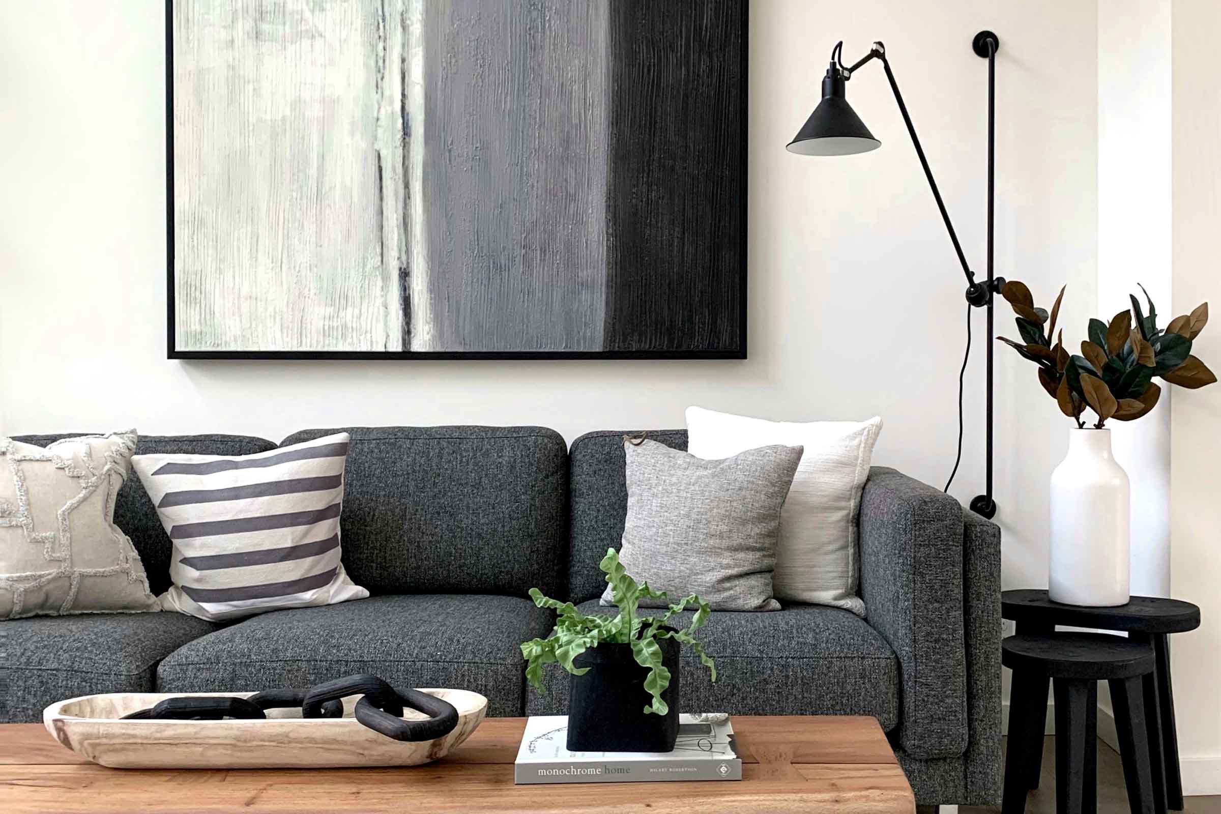 Living luminos cu canapea gri, perne, artă modernă, lampă și măsuță laterală