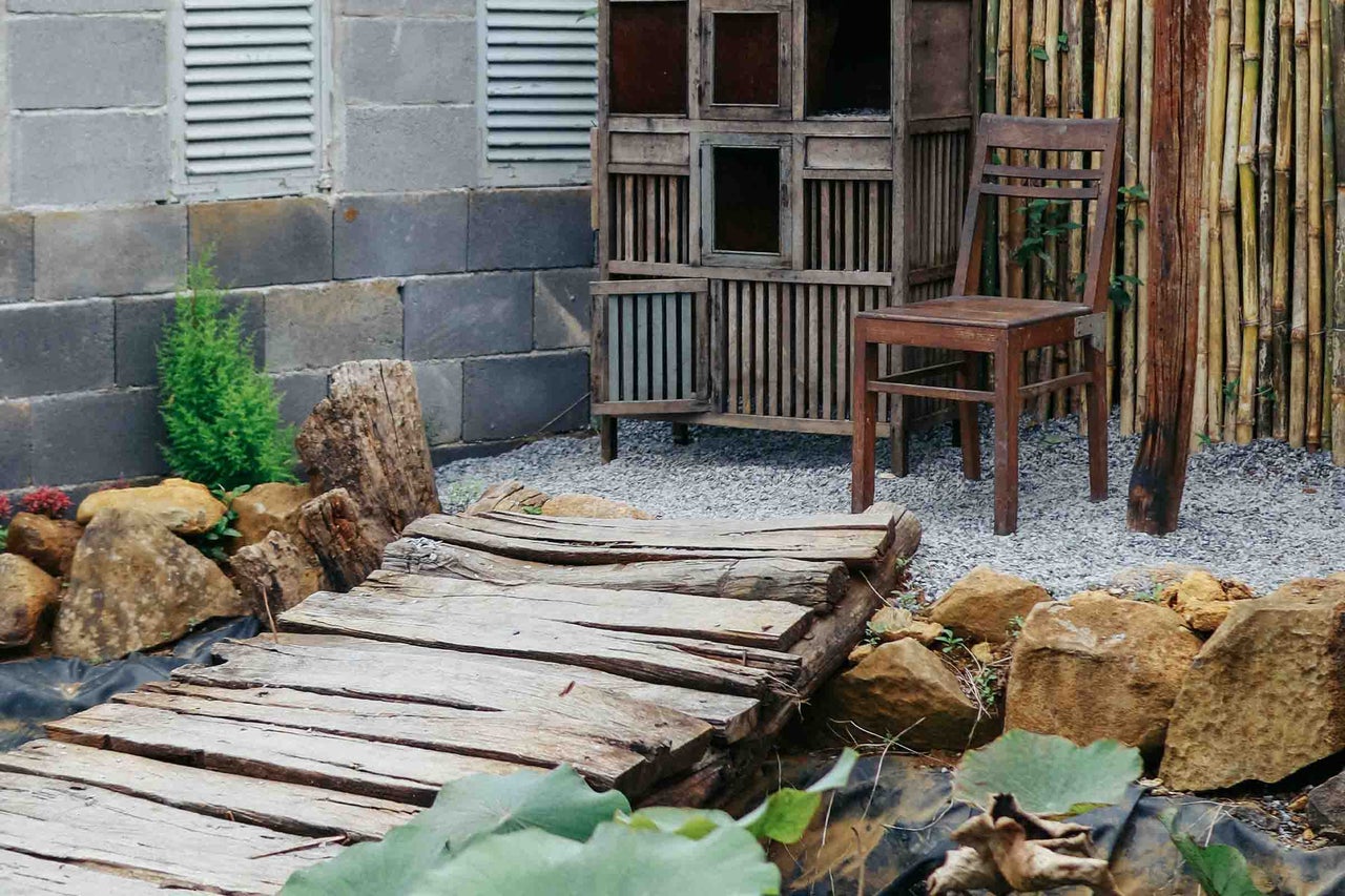 Design de grădină rustic cu pod de lemn, dulap vechi din lemn și scaun în fața unui zid din blocuri de beton și gard de bambus.