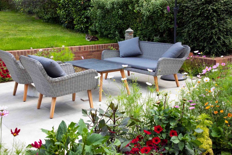 Set mobilier grădină cu canapea de două locuri, două fotolii și măsuță din ratan sintetic gri cu picioare din lemn pe o terasă luminoasă.