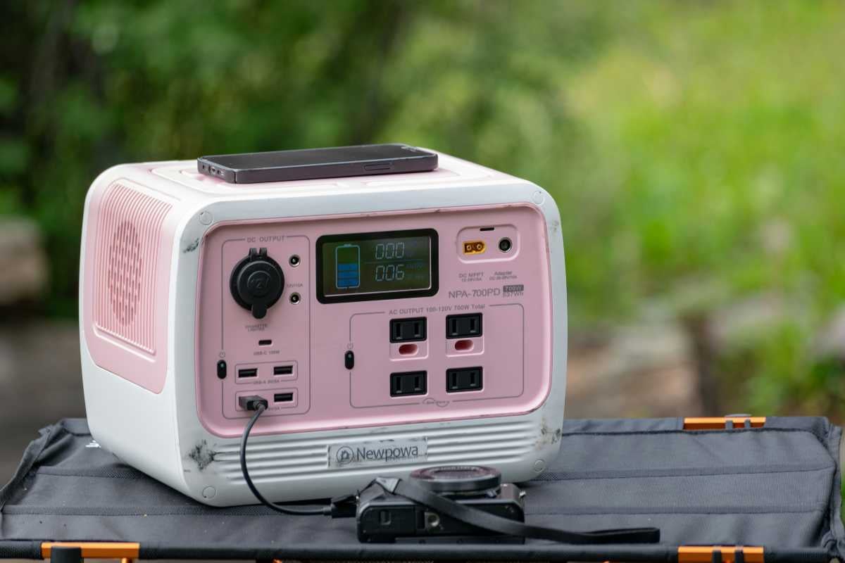 Stație de alimentare portabilă Newpowa cu diverse ieșiri, afișaj și un telefon mobil deasupra