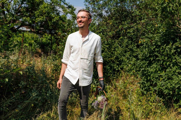 Un bărbat cu ochelari ține un coș cu plante în grădină.