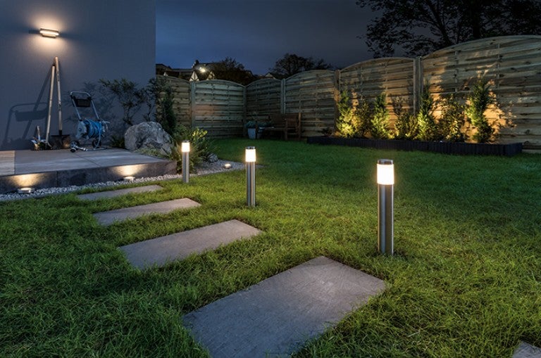 Grădină iluminată noaptea cu plăci de pavaj și lămpi de stâlp