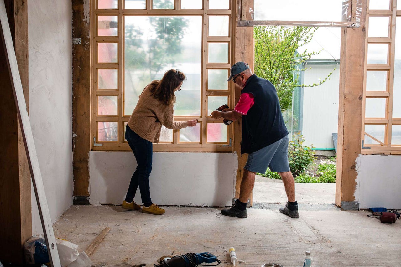 Persoane care construiesc o fereastră de lemn într-o cameră.