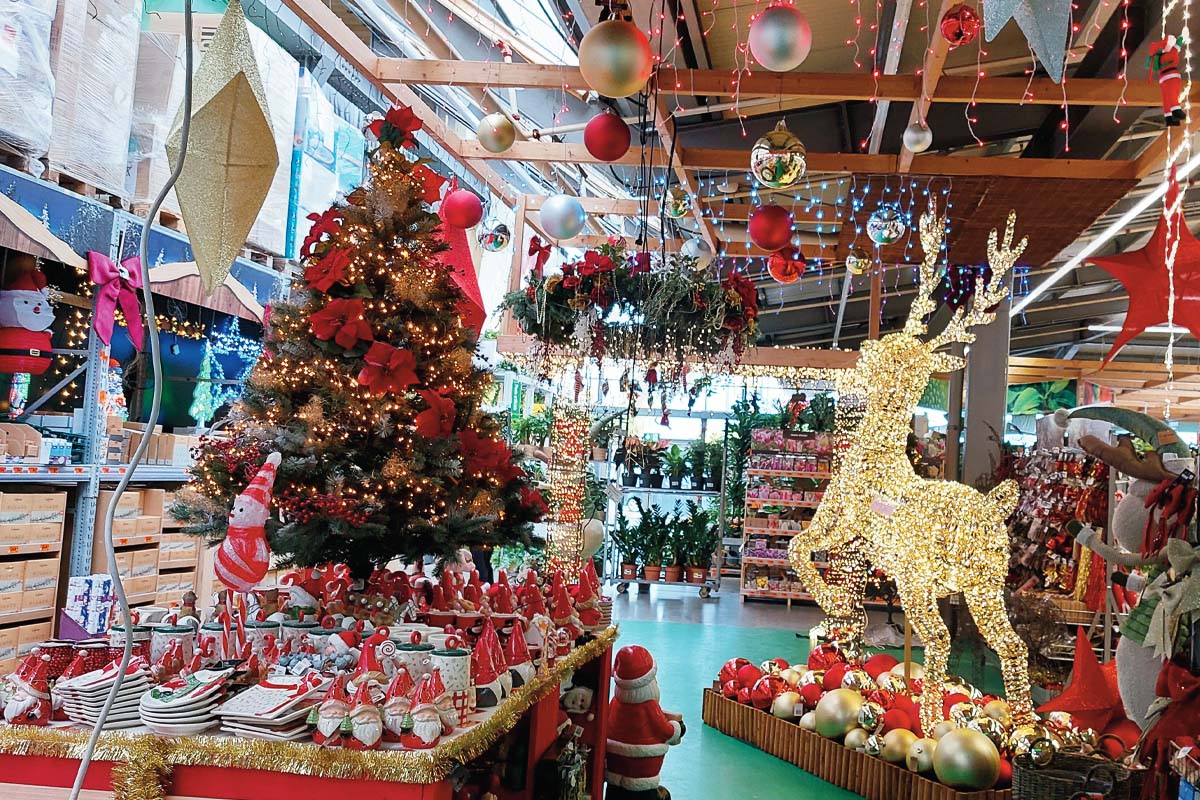 Decorațiuni de Crăciun într-un magazin de bricolaj cu brad împodobit, figurină ren luminată, globuri și articole festive în zona de vânzare.