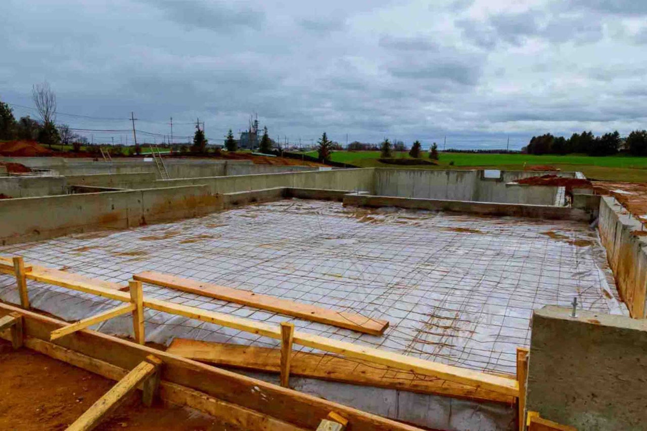Șantier cu fundație de beton, barieră de vapori, plasă de armare și cofraje din lemn pentru placa de fundație.