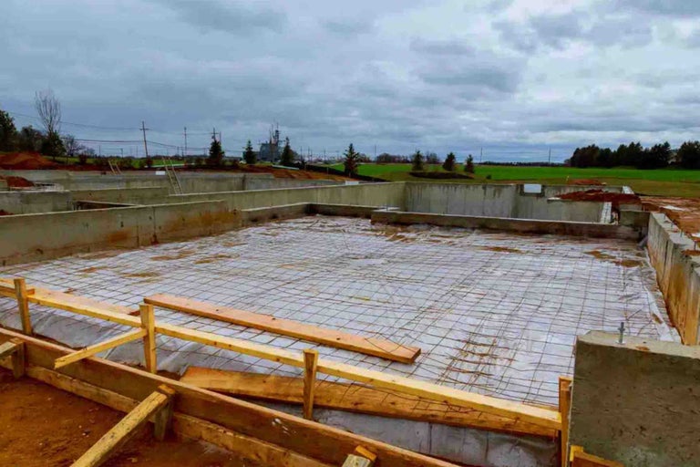 Șantier cu fundație de beton, barieră de vapori, plasă de armare și cofraje din lemn pentru placa de fundație.
